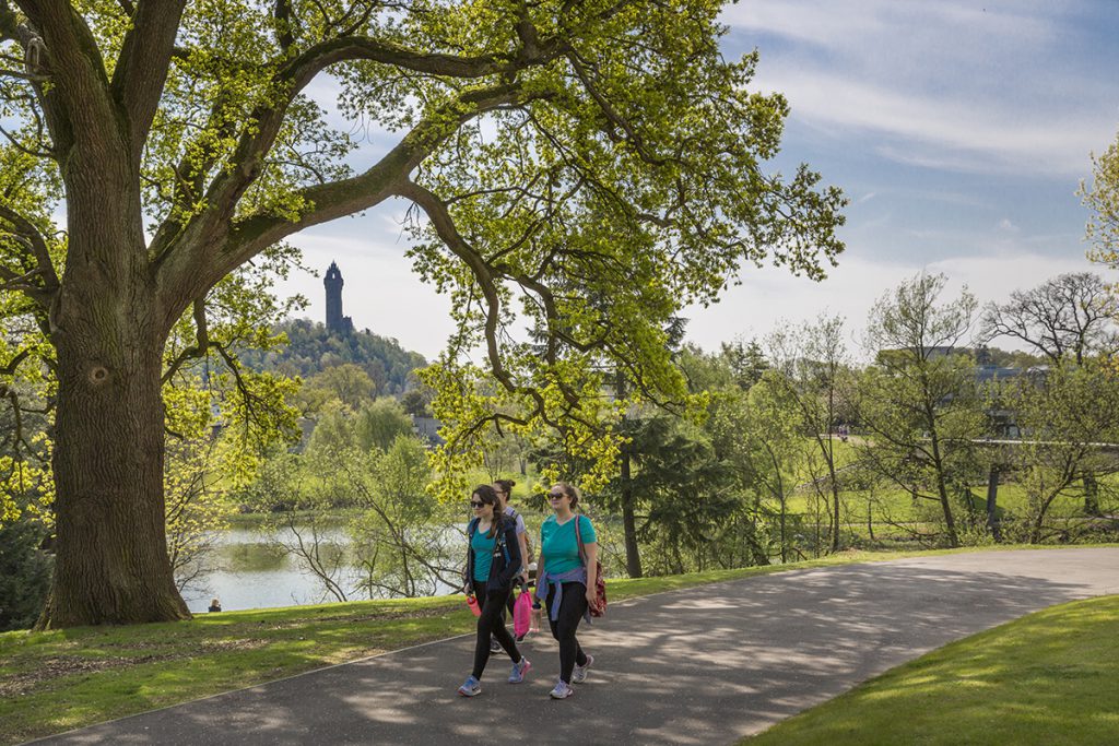 Woman walking around Airthrey Loch at Stirling University, Wallace Monument in background