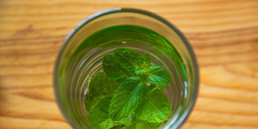 glass of water with mint leaves on wooden table
