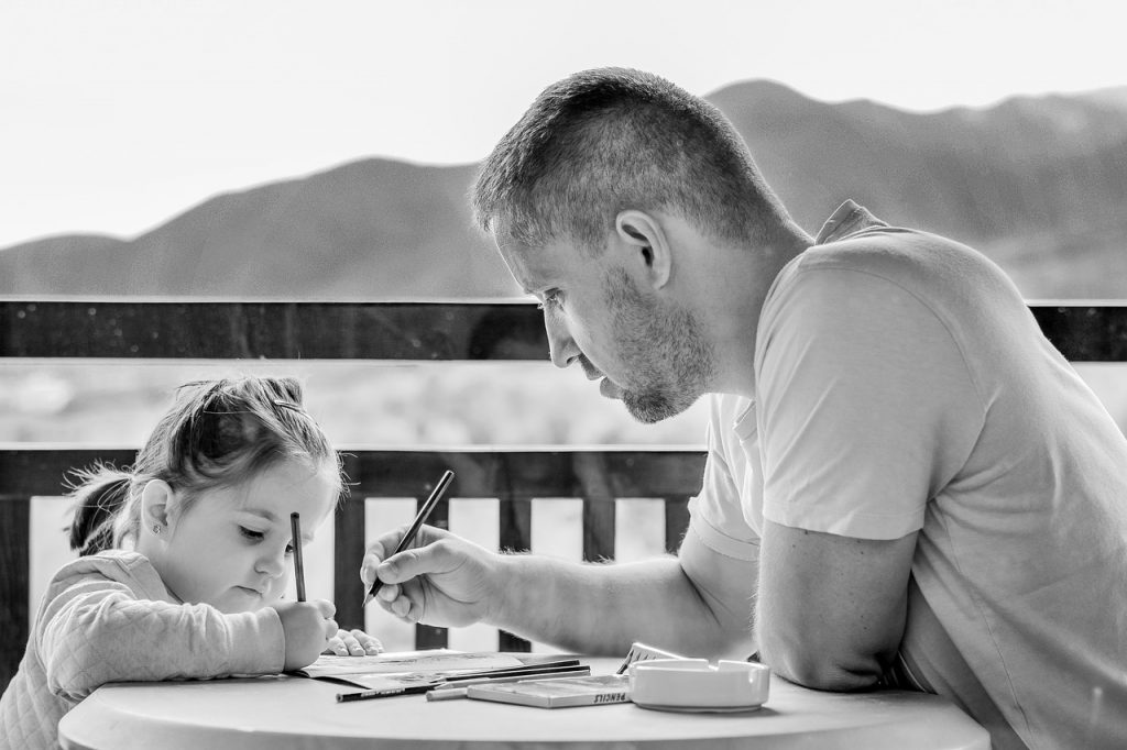 Dad sitting at table helping daughter to draw