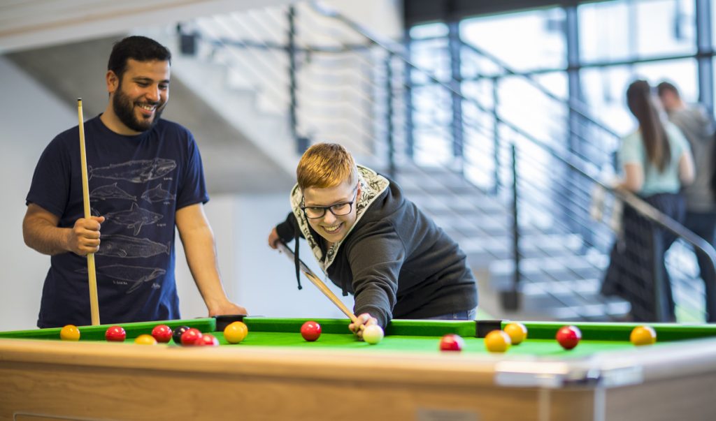 Students smiling playing pool in one of our student accommodations on campus